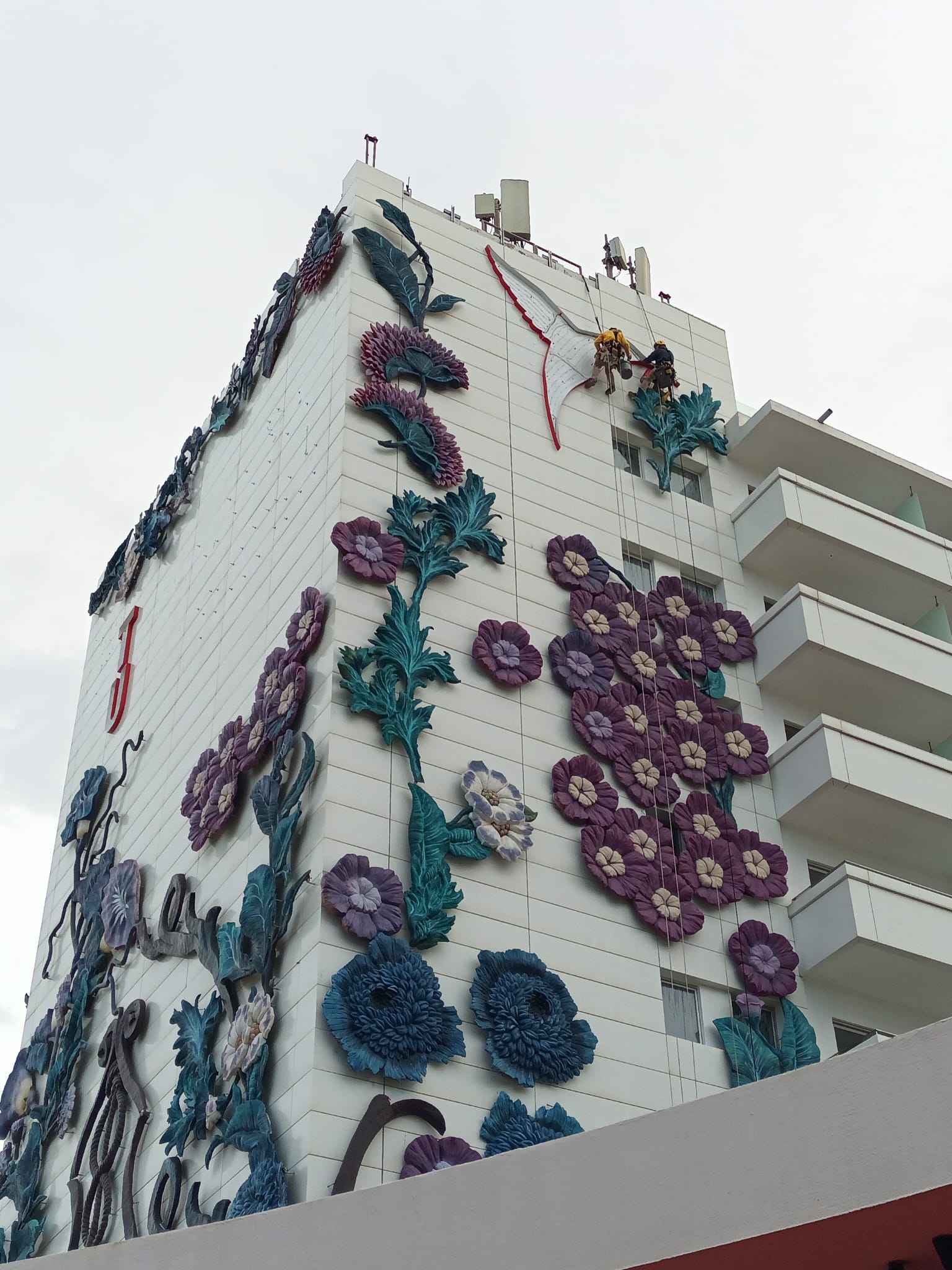 Dos técnicos trabajando con cuerdas en una fachada decorada con flores