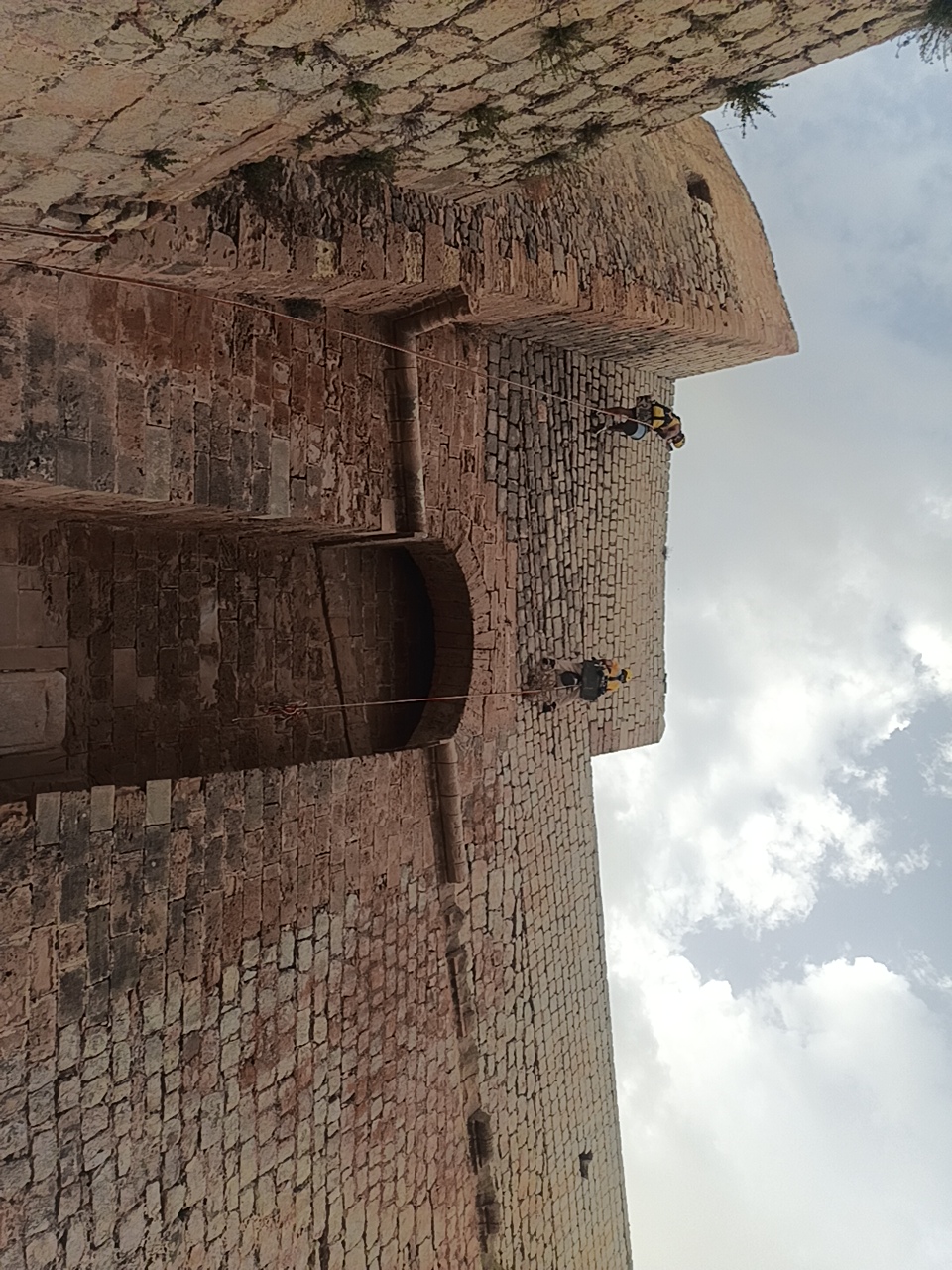 Dos técnicos retirando vegetación mediante cuerdas en la muralla renacentista de Ibiza